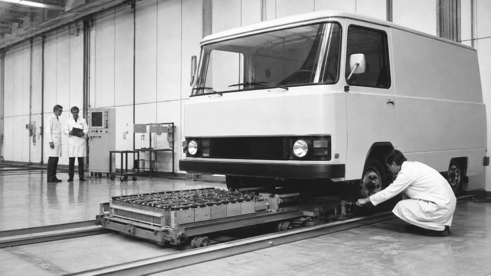 Delivery van standing above a battery pallet on rails in a hall