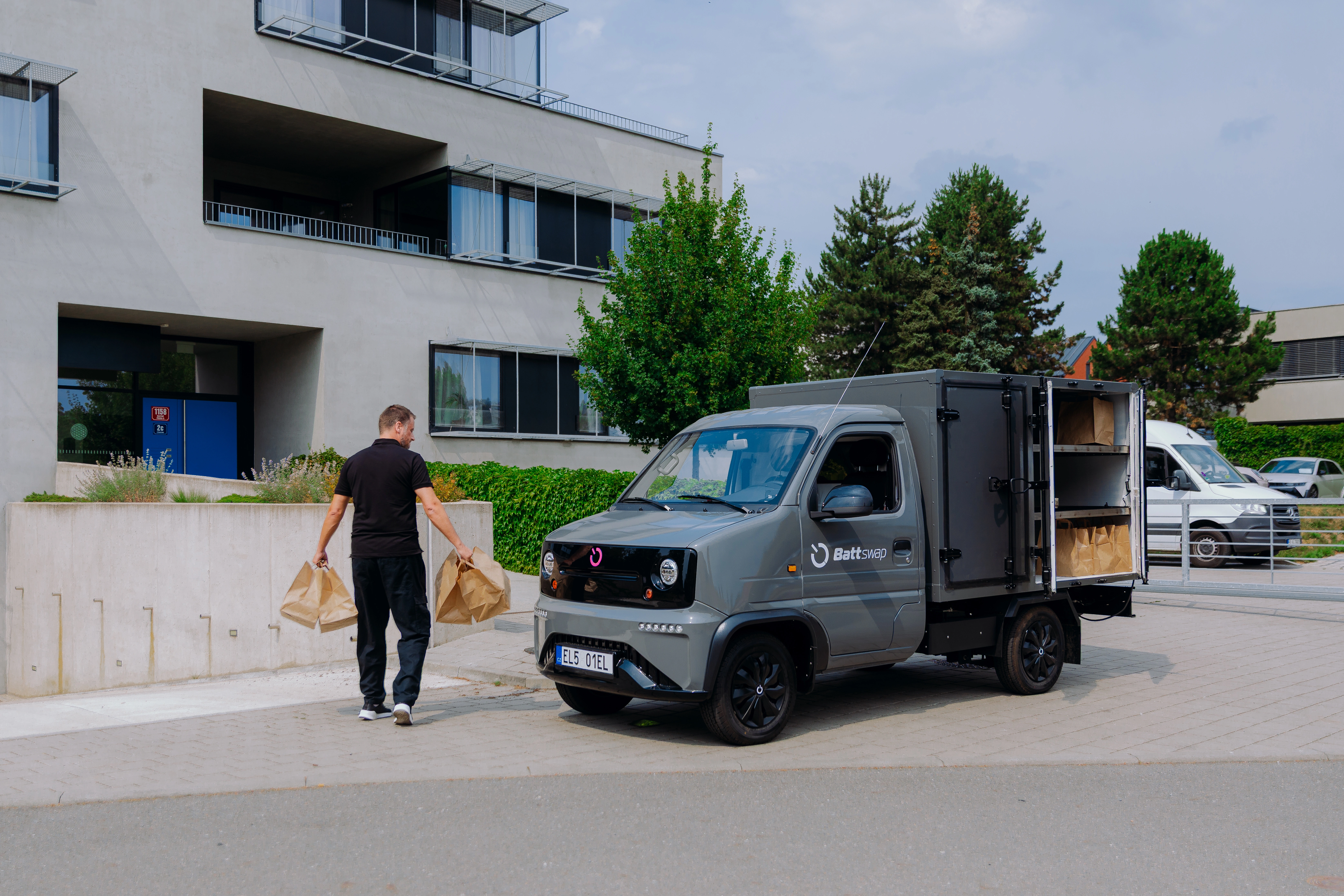 A courier carrying two paper bags away from a parked Battswap van with its cargo box open